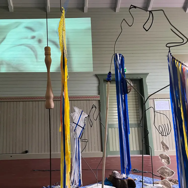 Installation med hängande objekt, textila band och projicerad bild i ett ljust rum.