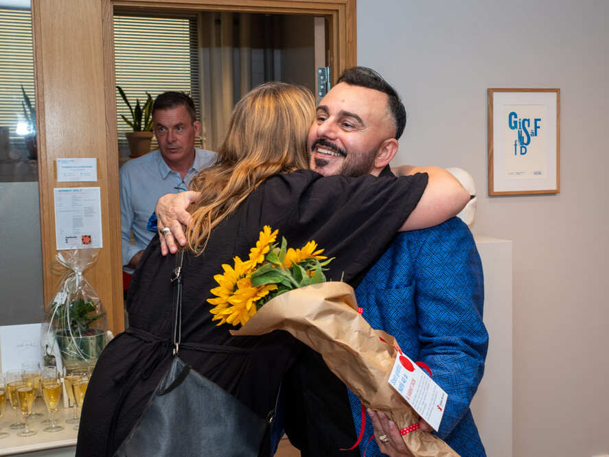 Två personer kramas under ett firande, den ena håller en bukett blommor