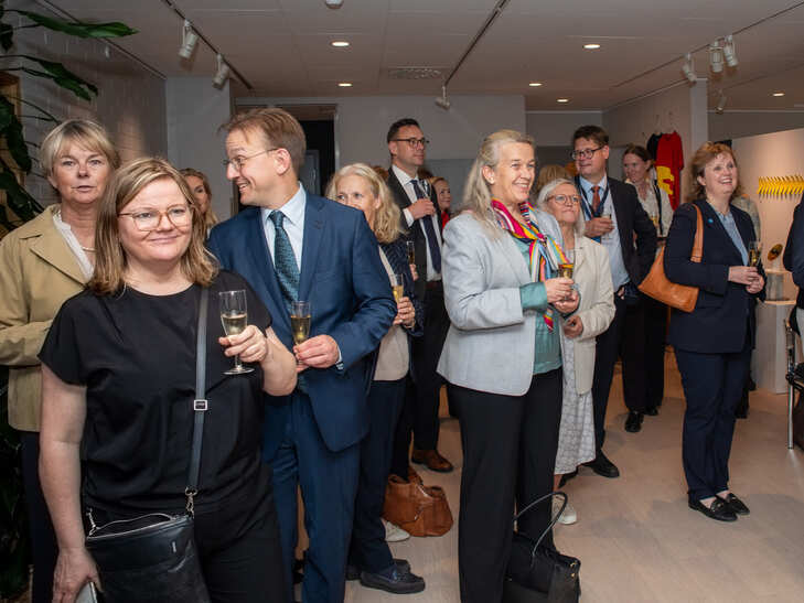 Grupp människor minglar och håller glas under ett arrangemang i en ljus lokal.