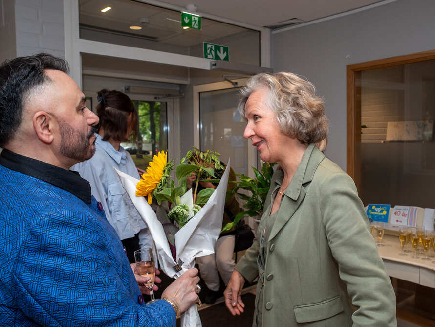 Två personer samtalar nära en entré, den ena håller en bukett blommor.