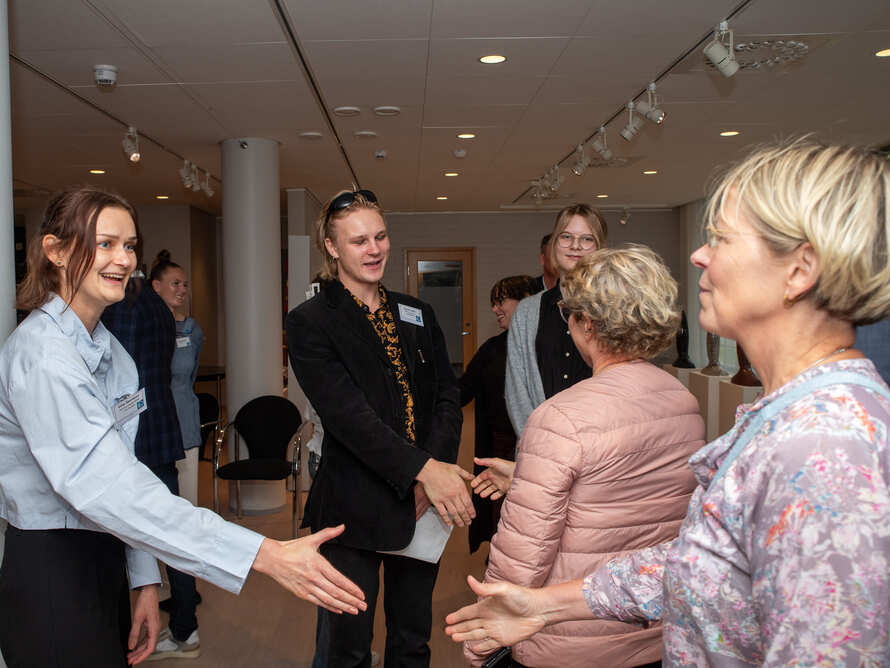 Människor hälsar på varandra med handslag i en ljus inomhusmiljö.
